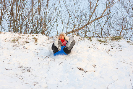 一个女孩坐在塑料浮冰上，正从积雪覆盖的滑梯上滚下来