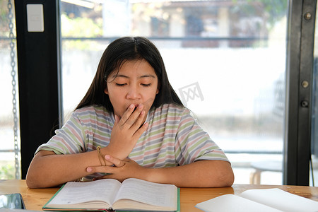疲倦摄影照片_女学生在看书时打哈欠感到疲倦无聊困倦。