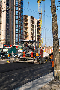摊铺机摄影照片_KYIV, UKRAINE - September 10, 2020：工业沥青摊铺机在街上的道路施工现场铺设新鲜沥青。