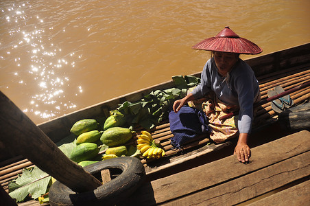 插图水果摄影照片_缅甸因勒 — 2015 年 11 月 29 日：在带绿色蔬菜的船上的少数民族妇女，在当地市场附近的带绿色水果的船上的少数民族高级妇女上方
