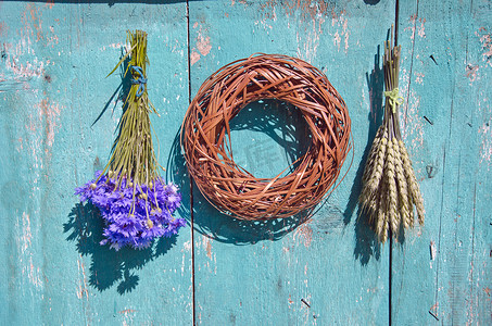 柳条花环摄影照片_农场墙上的小麦、矢车菊和木花圈