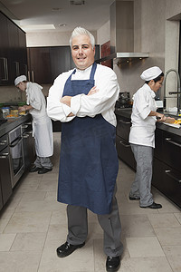 潮男摄影照片_自信的男厨师与在商业厨房工作的同事的全长肖像