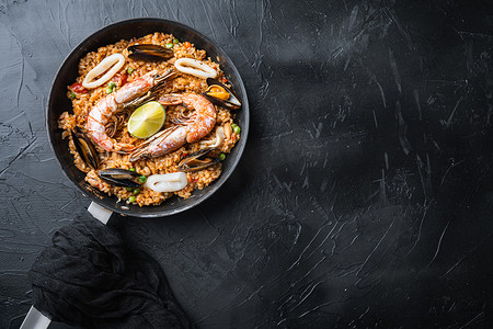 海鲜饭传统西班牙菜在煎锅中供应，在黑色纹理表面上，顶部视图有文字空间