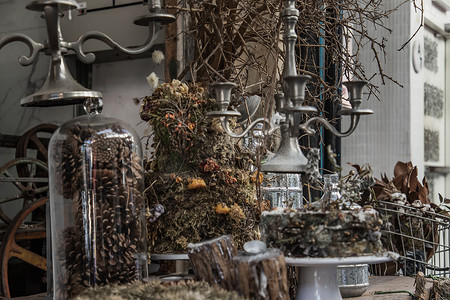 玻璃瓶装饰摄影照片_古色古香的烛台和干植物、干花、带玻璃瓶的松果装饰在咖啡馆的木桌上。