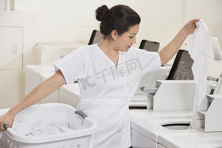 衣服放洗衣机摄影照片_将衣服放入洗衣机的年轻女员工