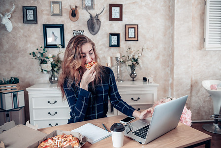 忙碌的女商人在家工作，一边用笔记本电脑在桌上工作，一边吃饭，女商人企业家在家工作，认真地沟通忙碌的任务。