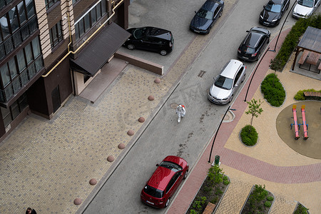 May摄影照片_UKRAINE, KYIV - May 20, 2020：身穿白色防护服和面具的男子走在街上，在冠状病毒流行期间对建筑物内表面进行消毒。