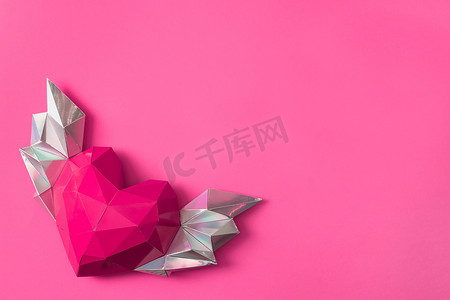 粉色多边形摄影照片_粉红色的多边形纸心，粉红色的背景上有翅膀。