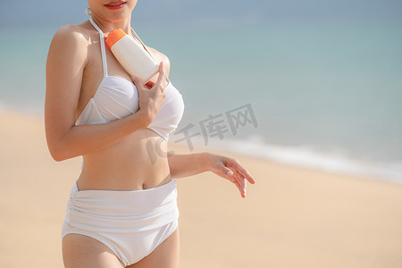 穿着白色比基尼的女人在沙滩上手拿防晒瓶。
