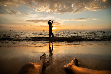 日落时分在沙滩上的女人剪影与男人的腿