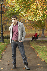 十几岁的男孩站在秋天的公园里，长凳上有女性形象