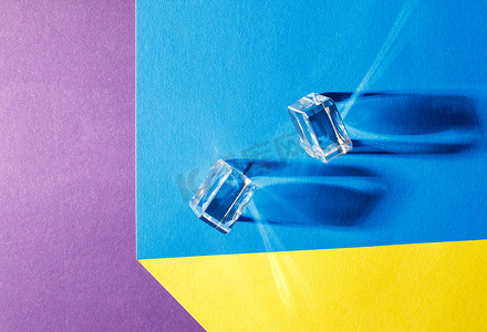 彩色透明立方体摄影照片_彩色桌子上的两个玻璃立方体