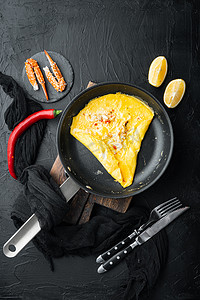 炸早餐煎蛋卷配蟹肉和奶酪，在煎铁锅上，黑色背景，顶视图平躺