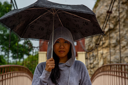 撑着雨伞摄影照片_年轻的亚洲女人在雨天撑着雨伞穿过一座木桥。