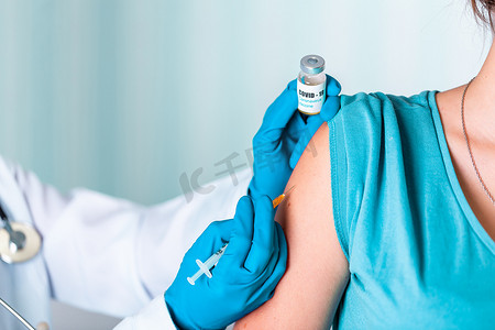 身着制服和手套的医生或护士在实验室制作带有 COVID-19 冠状病毒疫苗标签的注射疫苗瓶