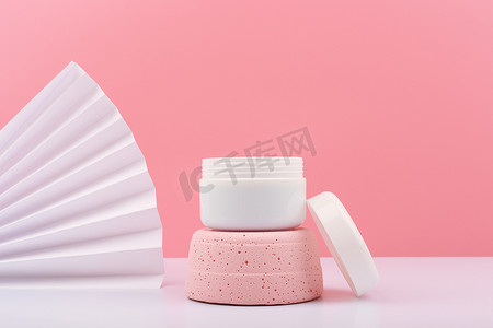 粉红色石膏讲台上白色打开的化妆品罐，粉红色背景，有波纹和复制空间
