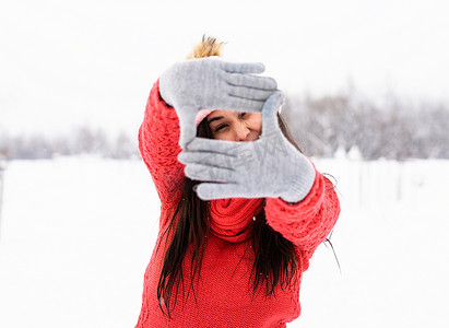 雪天，身穿红色毛衣的漂亮年轻女子在户外用手做框标