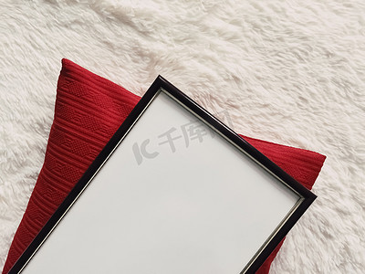带有空白复制空间的黑色薄木框作为海报照片打印模型、红色垫枕和蓬松的白色毯子、平躺背景和艺术产品