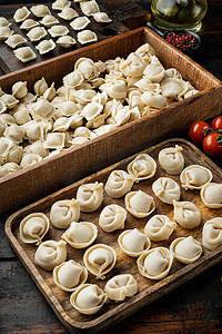 生饺子摄影照片_生意大利馄饨配新鲜帕尔马干酪和罗勒，旧深色木桌背景上的西红柿