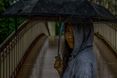 年轻的亚洲女人在雨天撑着雨伞穿过一座木桥。
