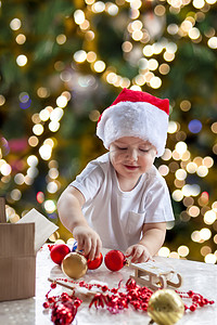 圣诞树亮摄影照片_小男孩从盒子里拿出圣诞玩具来装扮圣诞树。