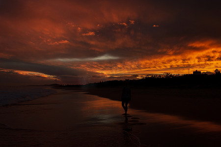 在澳大利亚阳光海岸的努萨维尔海滩，年轻女性在海滩上散步，背景是创辉日落。