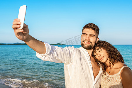 一对年轻恋人在日落或日出时穿着波西米亚夏装在海边度假时自拍。