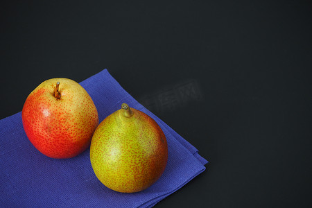 书斋画卷摄影照片_蓝色餐巾纸上的两个熟梨，特写，黑色背景。