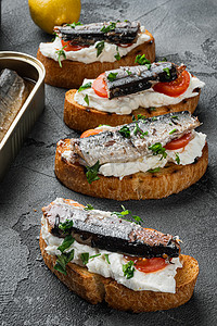 灰色石桌背景中的开放式三明治，配烤面包乳清干酪和鱼沙丁鱼