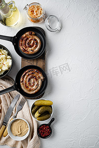 烧烤配菜摄影照片_铸铁煎锅中的传统德国香肠配土豆泥和酸菜，白色背景，顶视图平躺，有文本复制空间
