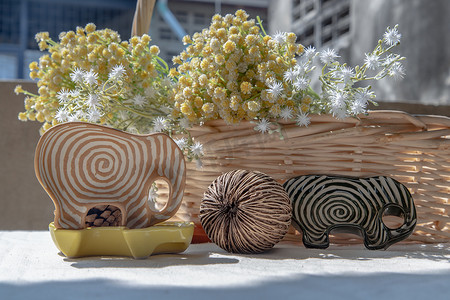 综艺奇葩说摄影照片_一套大象形状的陶瓷杯，里面有干的西伯利亚奇葩种子和编织篮子里的一束鲜花，用来装饰房子很漂亮。