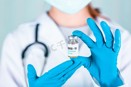 大药瓶摄影照片_女医生或护士穿着制服和戴面罩的手套在实验室拿着带有 COVID-19 冠状病毒疫苗标签的药瓶疫苗瓶