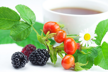 “一杯茶、黑莓、覆盆子和带叶子的玫瑰果浆果”