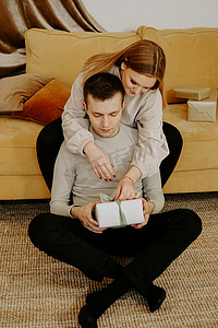 一对漂亮的年轻夫妇坐在家里的沙发上，手里拿着礼盒