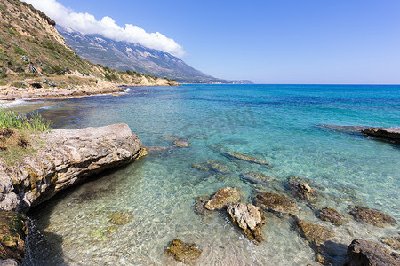 蓝色大海摄影照片_希腊有蓝色大海岩石和山脉的海岸