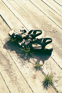 女式夏日凉鞋在温暖的阳光下，在带沙子和草的木板上，有免费的空白空间可供复制 — 休闲度假、夏季旅行和休闲的概念