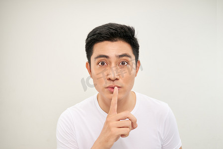 手指放在嘴里摄影照片_亚洲男人越过孤立的白墙，表现出沉默的手势，把手指放在嘴里