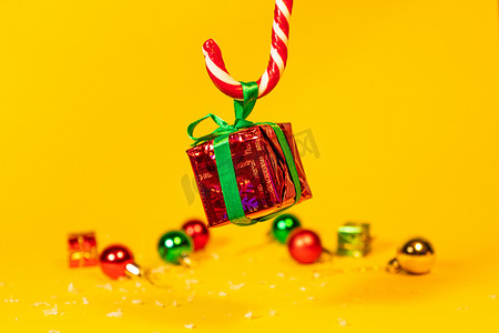 糖果手杖棒棒糖拿着一个礼盒，里面有黄色背景的圣诞礼物，圣诞糖果和新年装饰品。