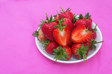 表面布满种子的草莓甜红果粉红色织物上白色盘子中的一组红色浆果心形水果