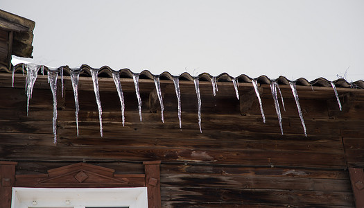 在寒冷多云的日子里，冰柱悬挂在木屋的屋顶上。
