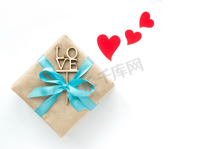 在棕色纸包裹的礼物盒与淡蓝色丝带和红色心脏在白色背景。