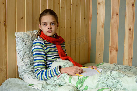 疲倦摄影照片_一个生病的女孩坐在床上，疲倦地看着窗外