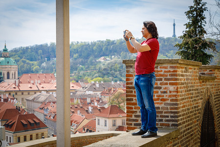 一个男人站在砖墙上拍摄布拉格的全景。
