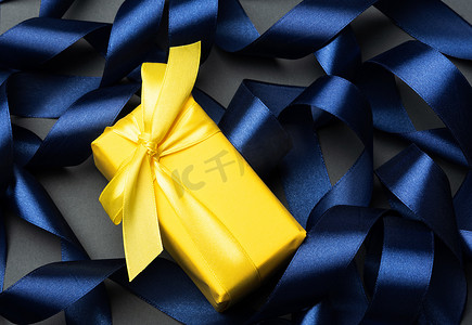 用黄色纸包裹的礼物在卷曲的蓝丝带背景，欢乐背景