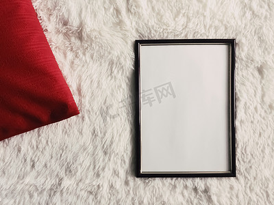 带有空白复制空间的黑色薄木框作为海报照片打印模型、红色垫枕和蓬松的白色毯子、平躺背景和艺术产品