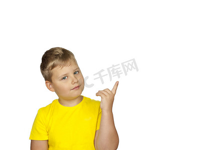 黄色信息摄影照片_一个身穿黄色 T 恤、白色背景的男孩用手指指着什么。