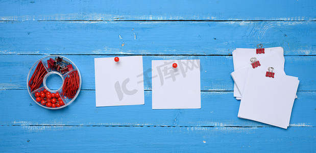 方形木质摄影照片_蓝色木质背景上带纸夹和夹子的空白方形纸和文具