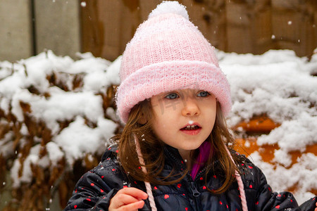 雪地里玩耍摄影照片_一个戴着粉色帽子的女孩在雪地里玩耍