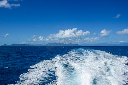 澳大利亚凯恩斯，在大堡礁潜水旅游的大船后面美丽的尾波，背景是蓝色山
