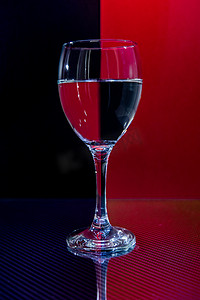 黑背景红摄影照片_玻璃碳反射面上有水的小玻璃杯，反射红黑背景
